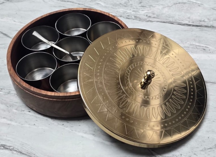 Open BittyJoy spice box showing seven stainless steel jars and a spoon inside a dark wood body, with the engraved brass lid resting alongside